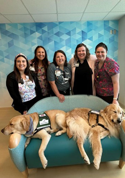 The Child Life Team standing behind a couch where two golden retriever therapy dogs are sleeping
